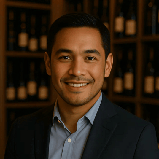 Professional portrait of Jim Hopper, wine cooling expert and author, standing in a wine cellar with neatly arranged wine bottles in the background.