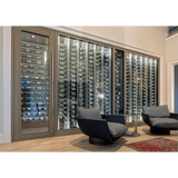 Glass-fronted wine wall with metal peg racking in a living room, cooled by a Wine Guardian cabinet system